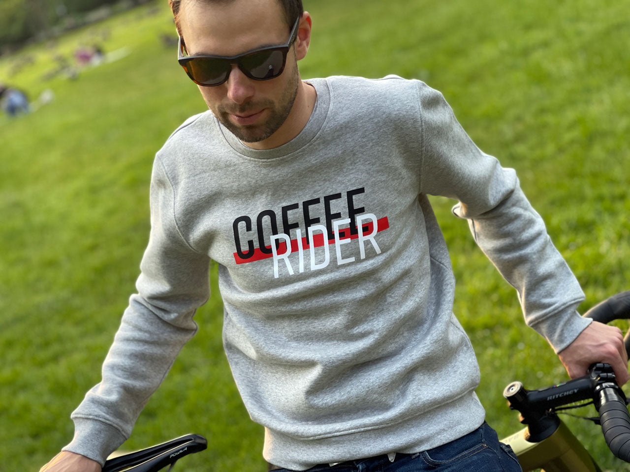 Eine Person steht auf einem Rasen mit einem grauer Pullover mit der Aufschrift Coffee Rider