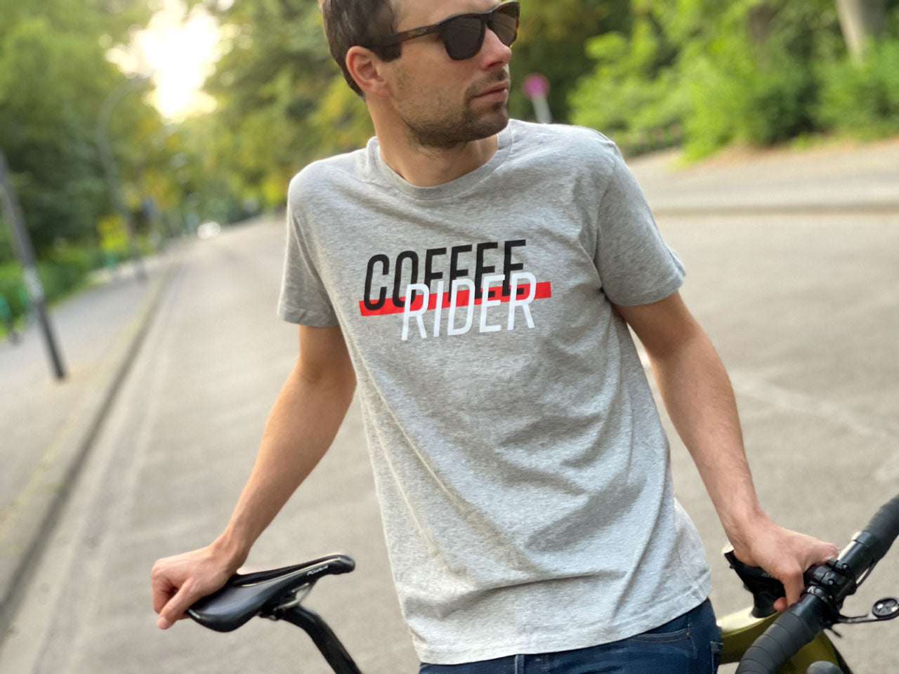 Eine Person steht mit einem grauen T-Shirt und der Aufschrift Coffee Rider auf einer Straße