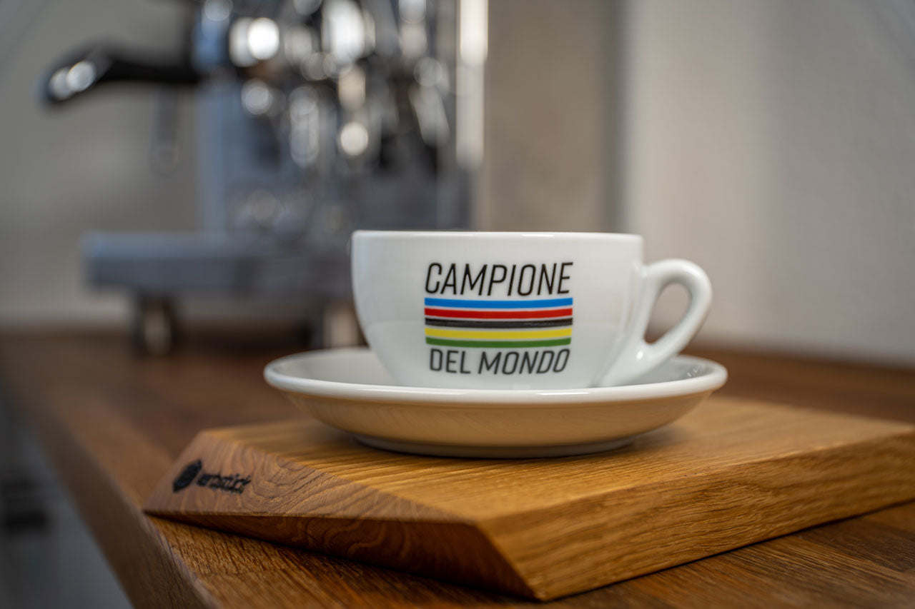 Eine weiße Cappuccino-Tasse mit fünf Streifen in Regenbogenfarben und dem Schriftzug Campione del Mondo.